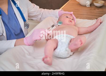 Un medico in uniforme controlla la bocca di un bambino con uno specchio. Il dentista esamina i denti di un neonato Foto Stock