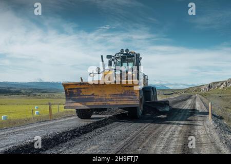 Livellamento o profilatura di strade di ghiaia su Islanda. Manutenzione ordinaria delle tipiche strade islandesi che non sono pavimentate con asfalto. Giornata di sole sul ghiaccio Foto Stock