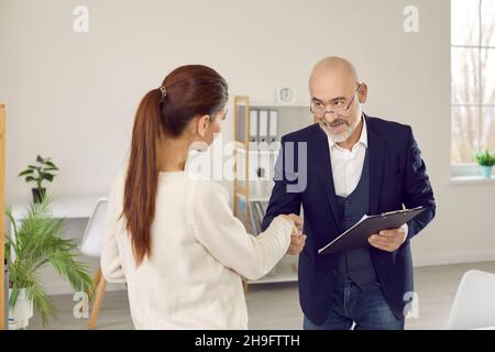 Lavoratore della banca, mediatore di prestito o agente immobiliare che si scambiano la stretta di mano con la giovane donna Foto Stock