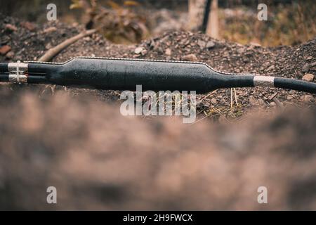 Collegamento di cavi ottici industriali, suddivisione a Y di un cavo, schermato in un contenitore in plastica visto scavato da terra o trincea in un cantiere. Foto Stock