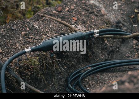 Collegamento di cavi ottici industriali, suddivisione a Y di un cavo, schermato in un contenitore in plastica visto scavato da terra o trincea in un cantiere. Foto Stock