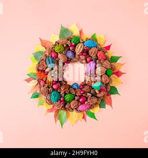 Decorazione a cerchio creativa autunno fatto di frutti di bosco di pietra e foglie colorate. Il concetto piatto di castagno e noci si basa su sfondo rosa pastello. Foto Stock