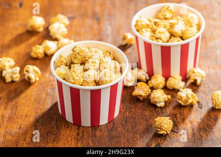 Popcorn caramello dolce in tazza di carta su tavola di legno. Foto Stock