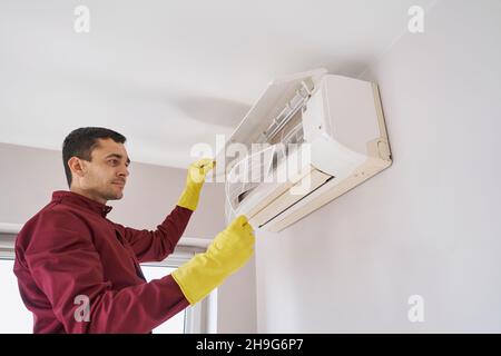 Uomo in guanti di gomma che ispeziona il componente dell'unità di climatizzazione Foto Stock