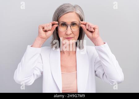 Foto di rigido bianco hairdo anziano donna indossare occhiali giacca isolato su sfondo grigio Foto Stock