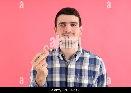 Il giovane uomo tiene gli apparecchi acustici su sfondo rosa Foto Stock
