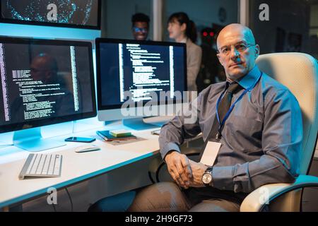Fidato manager maschile maturo dell'azienda IT-engineering seduto in poltrona sul posto di lavoro e guardando la fotocamera Foto Stock