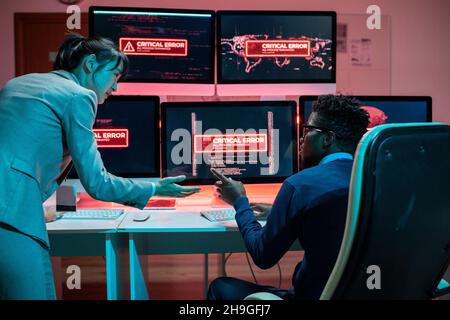 Due giovani programmatori interculturali che cercano di risolvere il problema dell'accesso ai dati interagendo di fronte ai computer Foto Stock