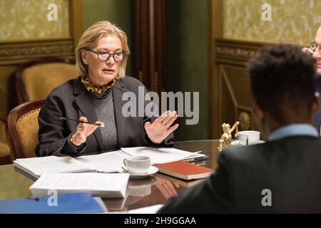 Fidata giurista bionda fidata che parla con la giovane collega maschile africana seduta davanti a lei Foto Stock