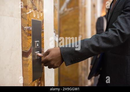 Mano di giovane uomo d'affari africano contemporaneo in abbigliamento formale premendo il pulsante per chiamare ascensore Foto Stock