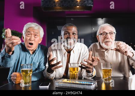 eccitati amici multietnici anziani gesturing mentre si guarda partita di calcio in birreria pub Foto Stock