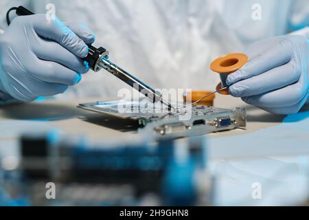 Mani di un tecnico con saldatore e latta che ripara la scheda madre del computer Foto Stock