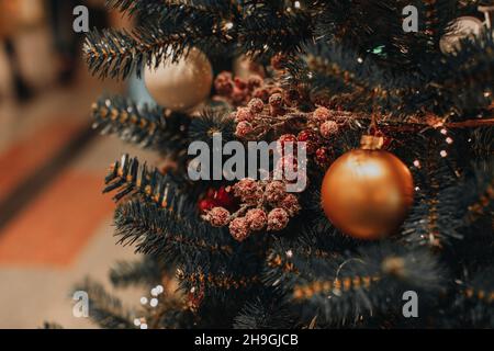 Sfera di Natale dorata e bacche rosse appesi sull'albero di Natale. Effetto bokeh magico. Sfondo festivo di vacanze invernali Foto Stock