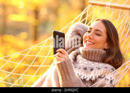 Donna felice rilassarsi su amaca cheking smart phone al tramonto in autunno