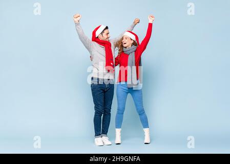 Ritratto a corpo pieno di felice coppia caucasica eccitata sorridendo e alzando le mani per celebrare il Natale in sfondo azzurro studio Foto Stock