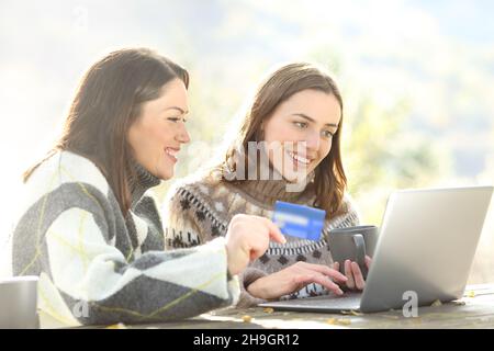 Due amici che acquistano online con il laptop e il credito si sono presi cura in inverno in un parco Foto Stock