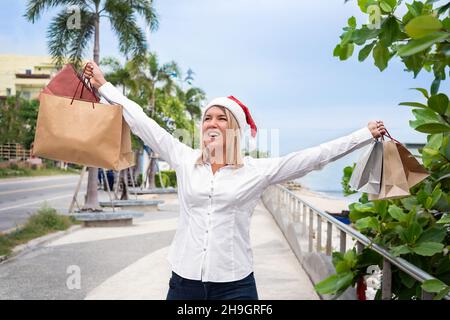 Ragazza in un cappello di Natale con una borsa shopping sulla strada del terrapieno Foto Stock