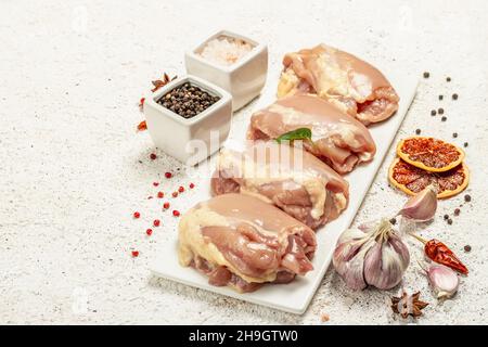 Coscia di pollo cruda senza ossa o pelle. Un ingrediente utile per preparare cibi sani, spezie, aglio. Sfondo di stucco chiaro, spazio di copia Foto Stock