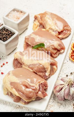 Coscia di pollo cruda senza ossa o pelle. Un ingrediente utile per preparare cibi sani, spezie, aglio. Fondo di stucco chiaro, primo piano Foto Stock
