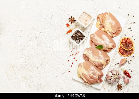 Coscia di pollo cruda senza ossa o pelle. Un ingrediente utile per preparare cibi sani, spezie, aglio. Stucco chiaro sfondo, vista dall'alto Foto Stock