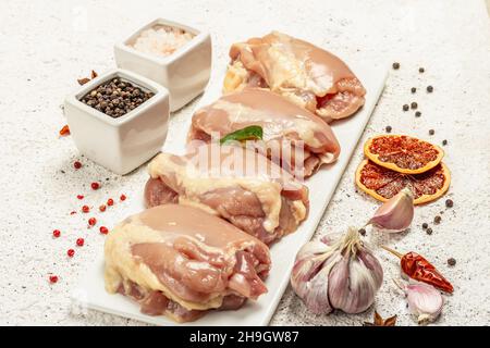 Coscia di pollo cruda senza ossa o pelle. Un ingrediente utile per preparare cibi sani, spezie, aglio. Fondo di stucco chiaro, primo piano Foto Stock