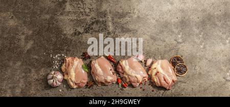 Coscia di pollo cruda senza ossa o pelle. Un ingrediente utile per preparare cibi sani, spezie, aglio. Sfondo di pietra scura, formato banner Foto Stock