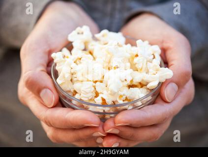 Donna mani che tengono ciotola di vetro pieno di popcorn. Primo piano Foto Stock