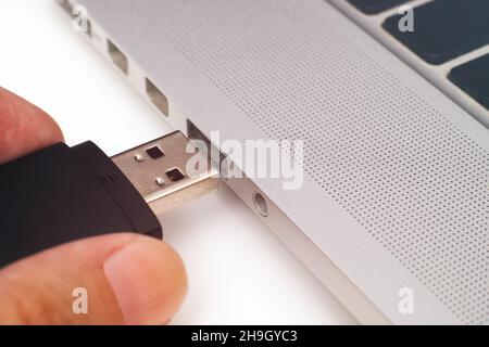 Una mano di una persona che inserisce un'unità flash USB in un computer portatile Foto Stock
