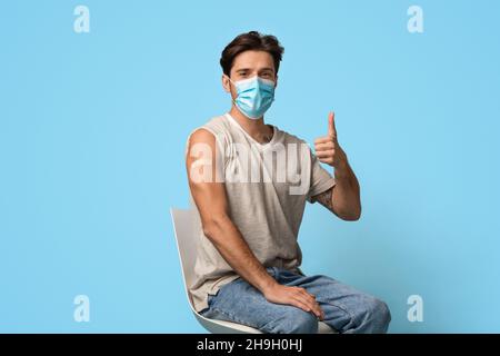 Uomo vaccinato che indossa la maschera che dimostra il braccio con il Plaster e che mostra il pollice in alto Foto Stock