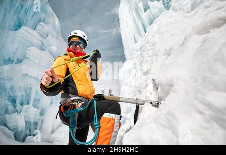 Ritratto di donna scalatore vicino a cascata ghiacciata con ascia di ghiaccio e nodo di corda in giacca arancione in montagna Foto Stock