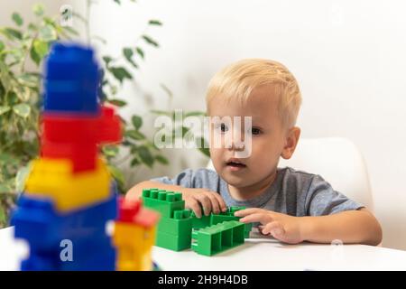 un ragazzo biondo seduto a un tavolo con giocattoli e guardando la macchina fotografica. Foto Stock
