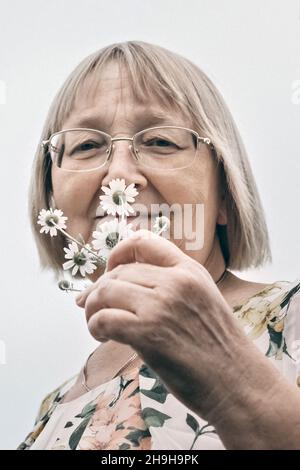Ritratto di una donna anziana che tiene un bouquet di fiori, odorando il profumo delle margherite. Autunno. Foto Stock