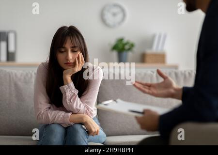 Infelice giovane signora araba che soffre di depressione, ascoltando consigli psicologo, seduto in ufficio medici, spazio copia Foto Stock
