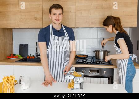 Giovane coppia in grembiuli per preparare la pasta con tagliatelle. La famiglia cucinando cibo vegano a casa. Concetto di stile di vita domestico, alimentazione sana, marria felice Foto Stock