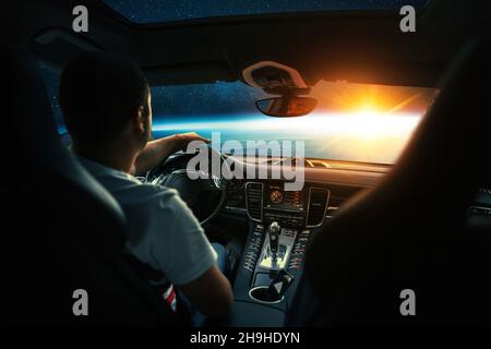 L'uomo si siede in un'automobile della navicella spaziale e vola al pianeta con un tramonto nello spazio. Viaggio spaziale in auto, concetto. Conducente dietro la ruota. Taxi interplanetario Foto Stock