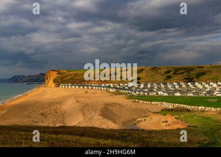 Un pozzo di luce solare autunnale illumina l'instabile East Cliff di arenaria e un enorme sito statico di casa mobile sulla Jurassic Coast a Burton Bradstock Foto Stock