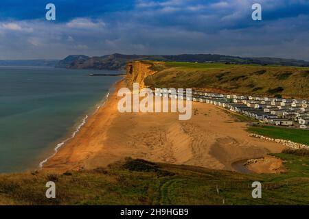 Un pozzo di luce solare autunnale illumina l'instabile East Cliff di arenaria e un enorme sito statico di casa mobile sulla Jurassic Coast a Burton Bradstock Foto Stock