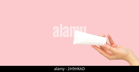 Mano donna che tiene bianco bianco tubo cosmetico di plastica su sfondo rosa. Banner con spazio di copia Foto Stock