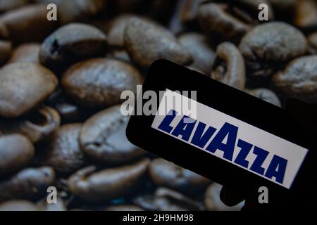 Rheinbach, Germania 1 ottobre 2021, il logo del marchio 'Lavazza' sul display di uno smartphone di fronte a una foto con caffè torrefatto in grani Foto Stock