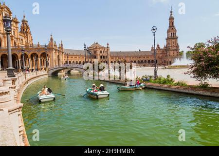 Siviglia, Andalusia, Spagna - 12 agosto 2021: Edificio rinascimentale centrale in piazza Plaza de Espana, vista sul fiume Guadalquivir con barche e gente Foto Stock