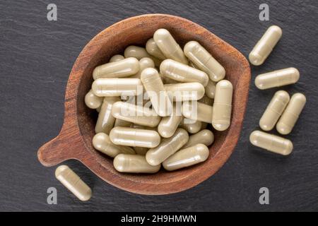 Parecchie pillole mediche in una ciotola di legno su una pietra di ardesia, primo piano, vista dall'alto. Foto Stock