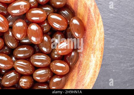 Parecchie pillole mediche in una ciotola di legno su una pietra di ardesia, primo piano, vista dall'alto. Foto Stock