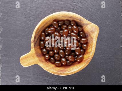 Parecchie pillole mediche in una ciotola di legno su una pietra di ardesia, primo piano, vista dall'alto. Foto Stock