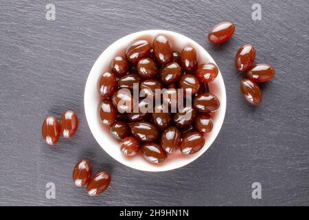 Diverse pillole mediche in una ciotola di ceramica bianca su una pietra di ardesia, primo piano, vista dall'alto. Foto Stock