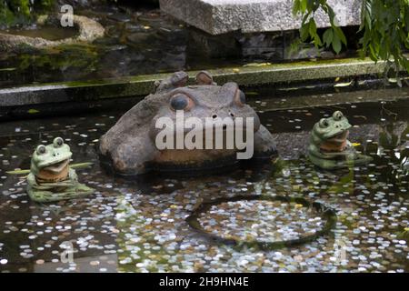 Primo piano delle statue di un rospo con due piccole rane in piscina Foto Stock