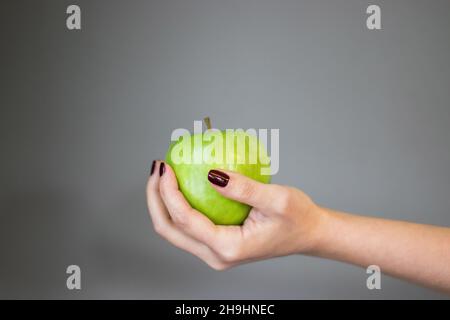 mela verde in piedi in mano della donna, su sfondo isolato Foto Stock
