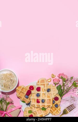 Cialde valentine a forma di cuore, con bacche e tazza di caffè latte su sfondo rosa. San Valentino, Mamma giorno dolce gustosa colazione idea Foto Stock