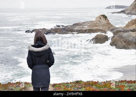 Una donna in piedi su una scogliera a Bodega Head, guardando fuori l'oceano, come visto da dietro. Foto Stock