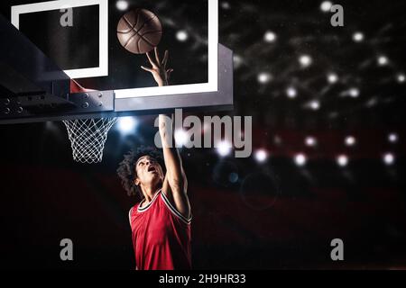 Giocatore di pallacanestro in uniforme rossa che salta in alto per fare un slam dunk al cesto Foto Stock