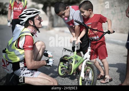 Steven Wright offre di lubrificare la catena ciclistica di un bambino nel campo profughi di Aida a Betlemme. Vedute generali di un viaggio in bicicletta per la Cisgiordania della Palestina organizzato dalla beneficenza britannica Medical aid for Palestinese nel 2015 Foto Stock